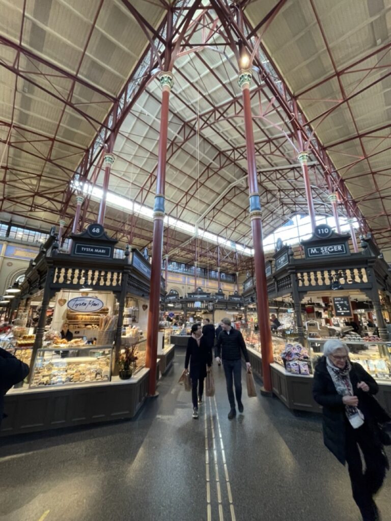 Plongez dans l'effervescence du marché couvert d'Ostermalm à Stockholm. Cette photo illustre l'atmosphère animée et colorée du marché, où les étals regorgent de produits frais et locaux. Des senteurs alléchantes se mélangent dans l'air, invitant les visiteurs à découvrir les saveurs de la cuisine suédoise. Les lumières tamisées et les arches en pierre créent une ambiance chaleureuse et accueillante, invitant les visiteurs à flâner et à découvrir les trésors culinaires de la ville. Le marché couvert d'Ostermalm est un lieu incontournable pour les gourmands et les curieux en quête de découvertes gustatives.