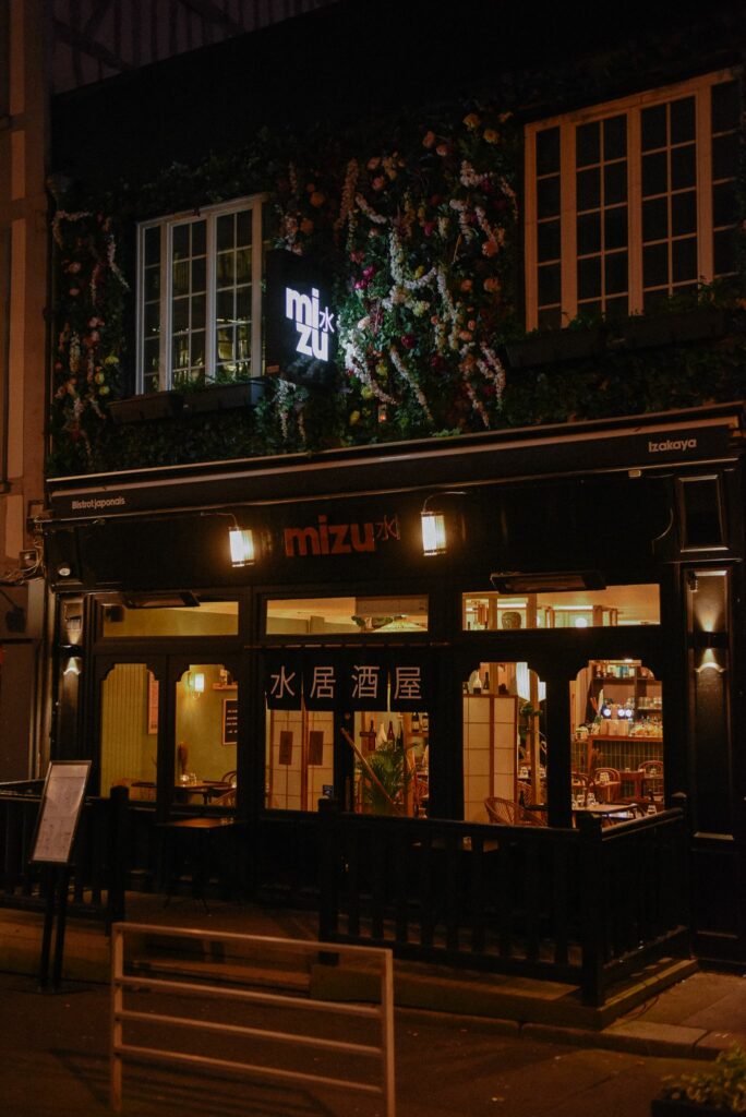 La devanture de Mizu de nuit est tout simplement magnifique ! Cette photo vous montre la façade du restaurant, éclairée par des lumières tamisées qui créent une ambiance chaleureuse et conviviale. Chez Mizu, vous pourrez déguster une cuisine japonaise authentique dans un cadre élégant et apaisant, qui invite à la détente et à la découverte. Que vous soyez en couple, entre amis ou en famille, vous serez accueillis avec le sourire chez Mizu pour passer une soirée inoubliable. Alors, n'hésitez plus, rendez-vous chez Mizu pour vivre une expérience culinaire et visuelle unique à Rouen !