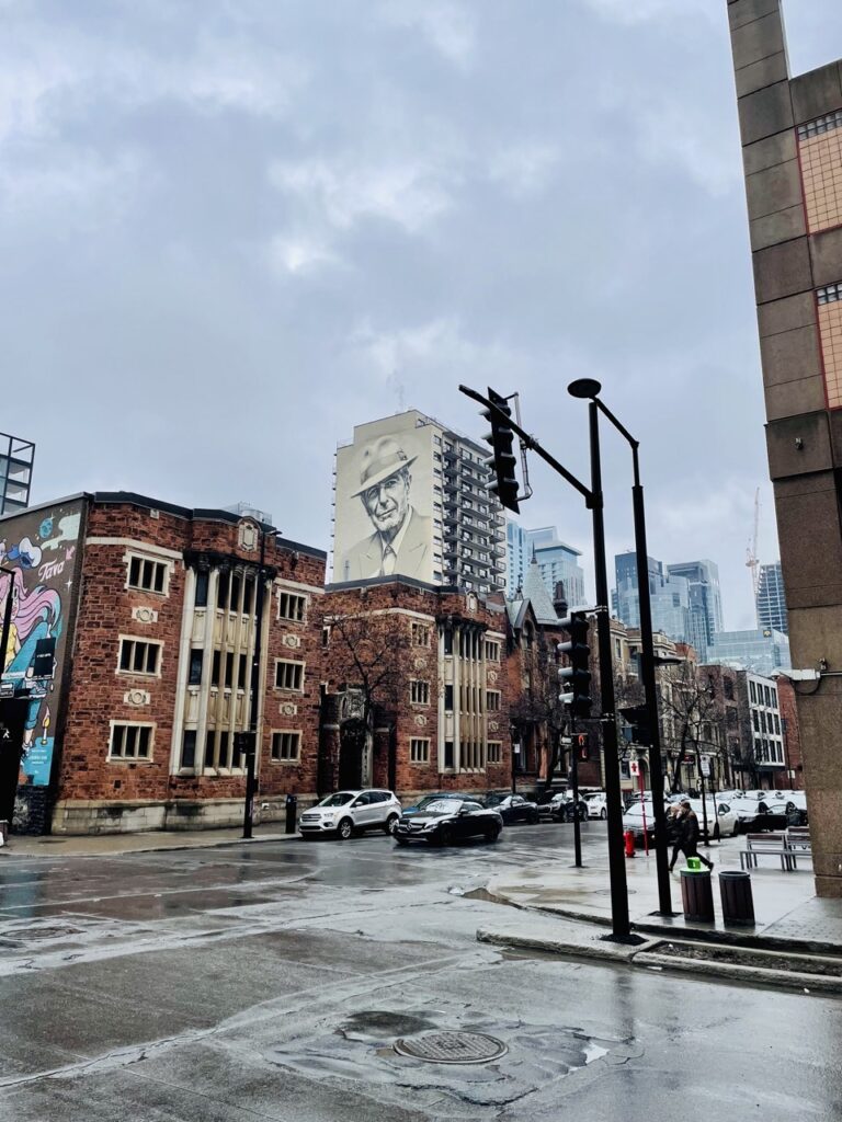 Ambiance urbaine au cœur du centre-ville de Montréal, avec un immeuble arborant une œuvre street art de Leonard Cohen.