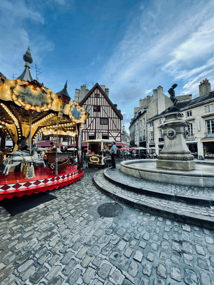 La majestueuse Place François Rude, nichée au cœur de la charmante ville de Dijon, se dévoile telle une œuvre d'art en plein air. Les façades élégantes des bâtiments, baignées de nuances chaudes de pierre, semblent figées dans le temps, rappelant l'histoire riche de cette ville. Les arbres matures offrent une ombre bienvenue, créant un havre de fraîcheur pendant les journées ensoleillées. Cette place pittoresque est un lieu incontournable pour tout voyageur en quête d'histoire, de culture et de beauté architecturale à Dijon. Chaque coin de cette place respire l'authenticité et l'élégance, invitant les visiteurs à flâner, à savourer un café en terrasse ou à simplement s'immerger dans l'atmosphère envoûtante de cette place.